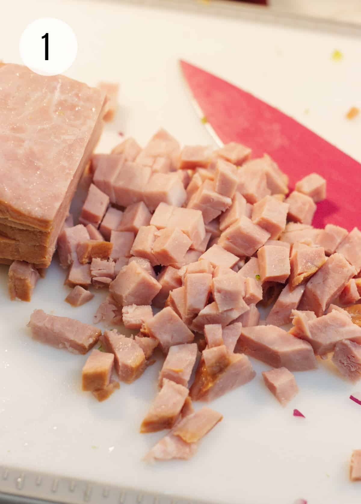 White cutting board with chopped cooked ham and pink chef's knife. 