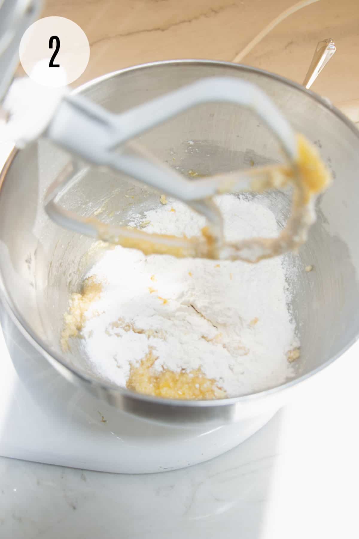 Butter sugar mixture with flour mixture for lemon cookies in a silver bowl mixed by a white mixer paddle.