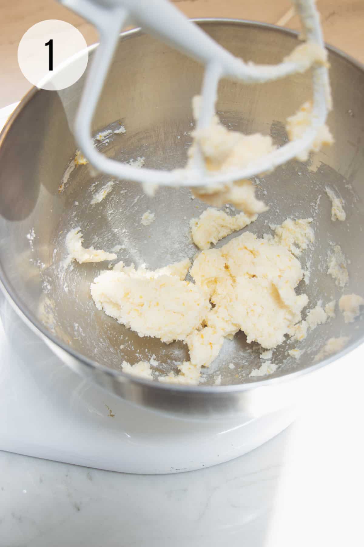 Butter and sugar being creamed in a silver bowl by white mixer paddle.