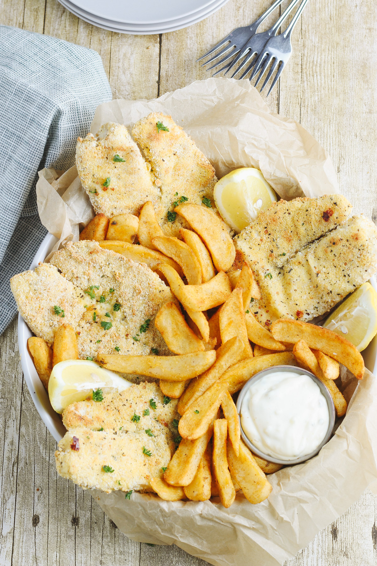 Bowl of breaded fish filets and French fries with lemon and parsley garnish and small bowl of tarter sauce.