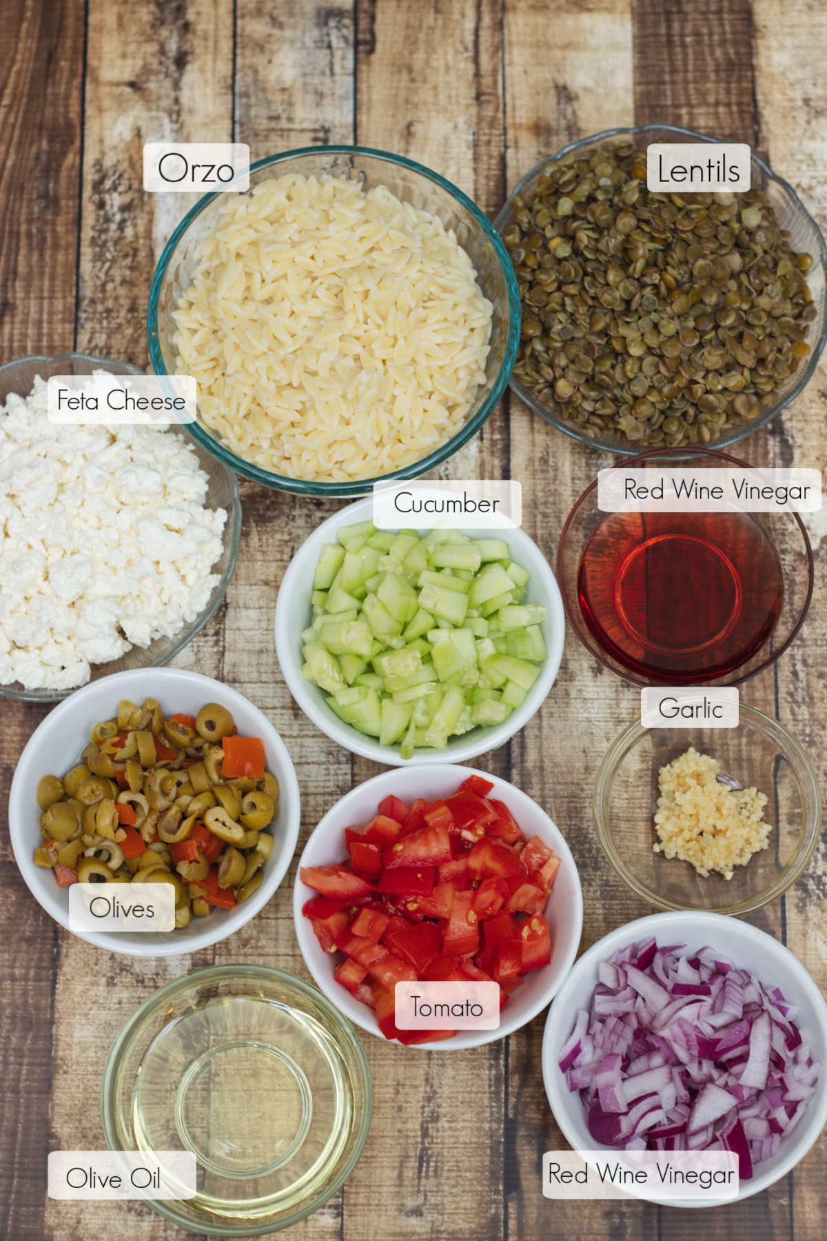 Image of ingredients in bowls with labels for Greek Orzo Salad with Lentils. 