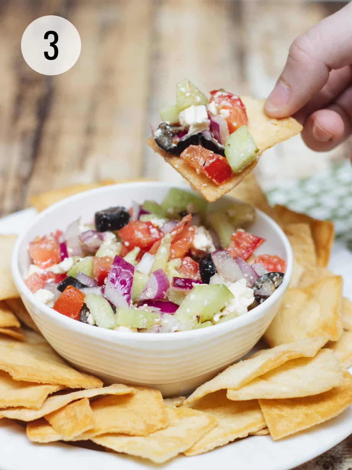 Greek salsa with tomatoes, cucumbers, black olives and feta cheese on a pita chip with white bowl of salsa and chips. 