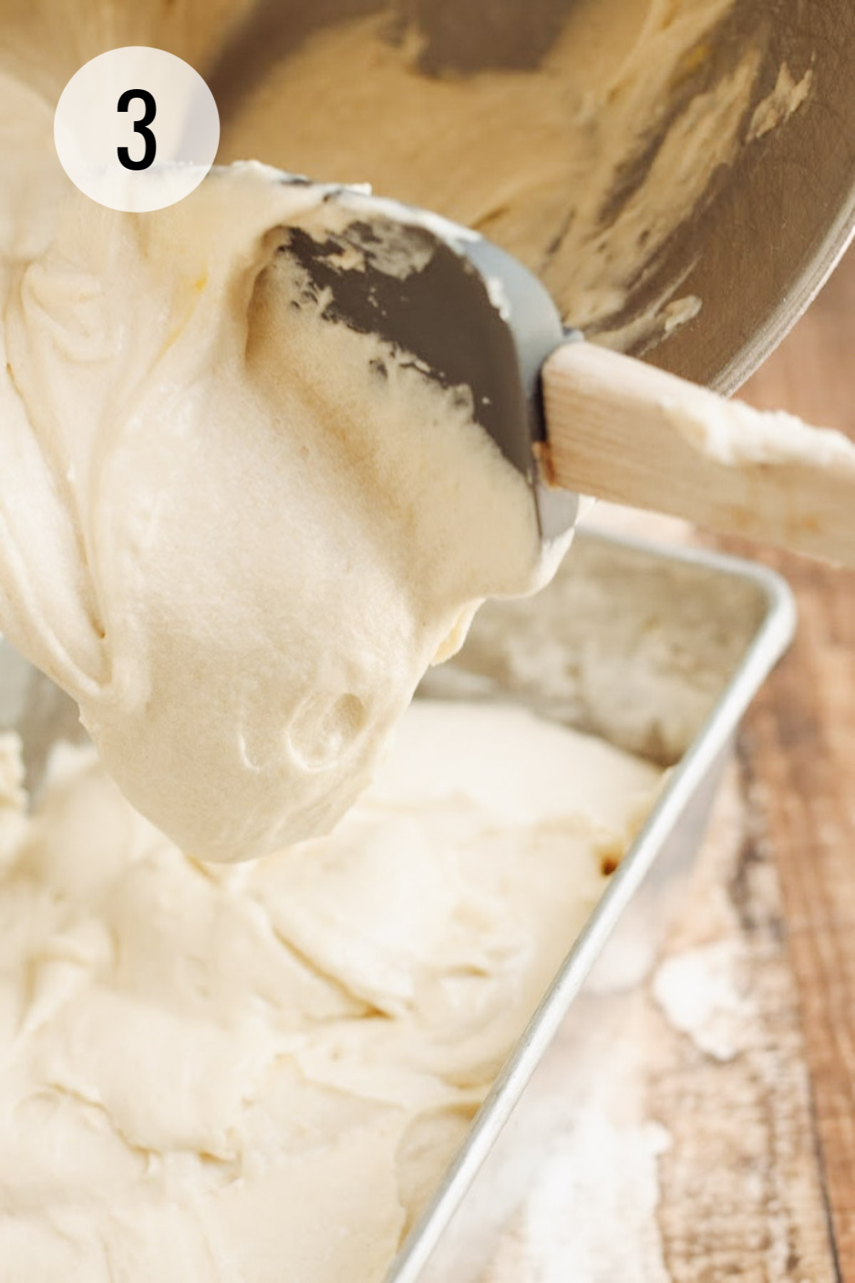 Pound cake batter being spread into a metal loaf cake pan using a grey rubber spatula.