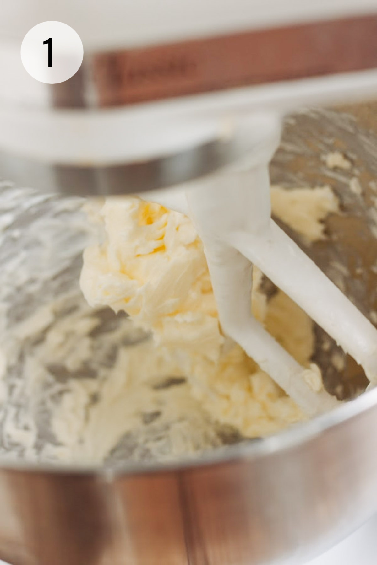 Butter and sugar being creamed in a silver bowl of a stand mixer with a white paddle beater. 