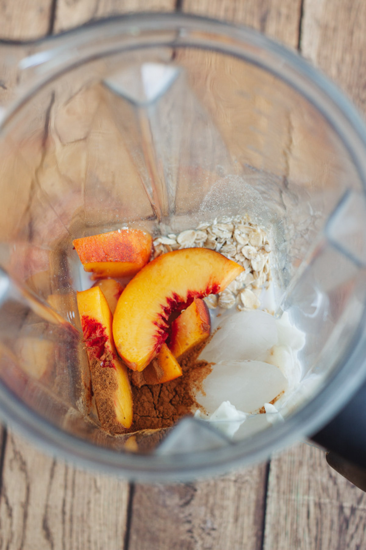 Top view into a blender jar with peaches and other ingredients to make a peach smoothie with yogurt. 