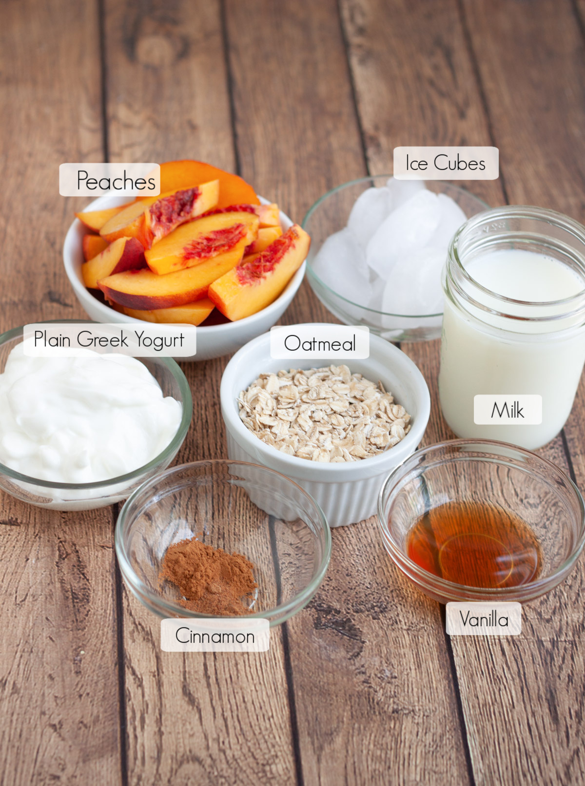 Ingredients in bowls with labels to make a peach pie smoothie with yogurt.