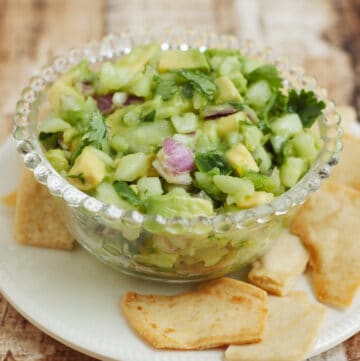 bowl of avocado cucumber salsa with pita chips on a white plate