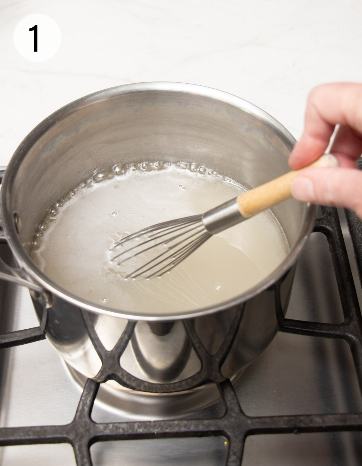 Boiling sugar water being whisked in a silver sauce pan. 