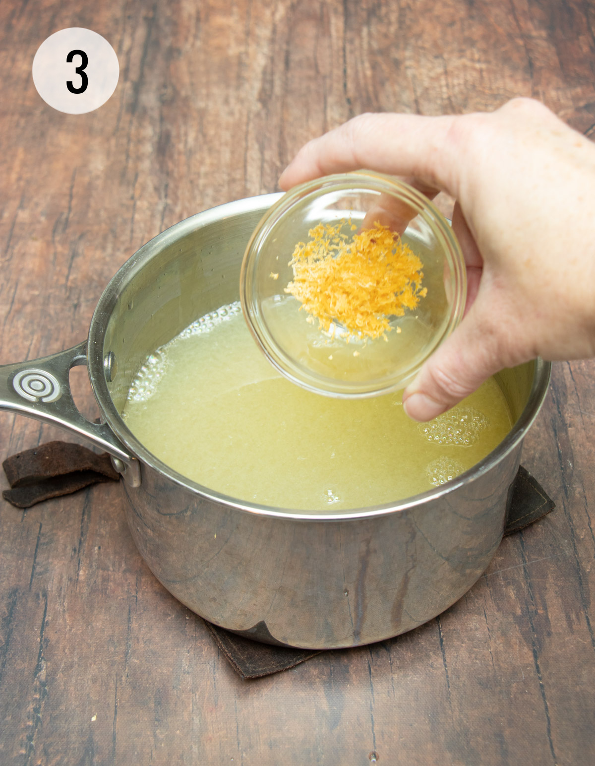 Pouring lemon zest from small bowl into sauce pan with lemon and sugar mixture for lemonade. 