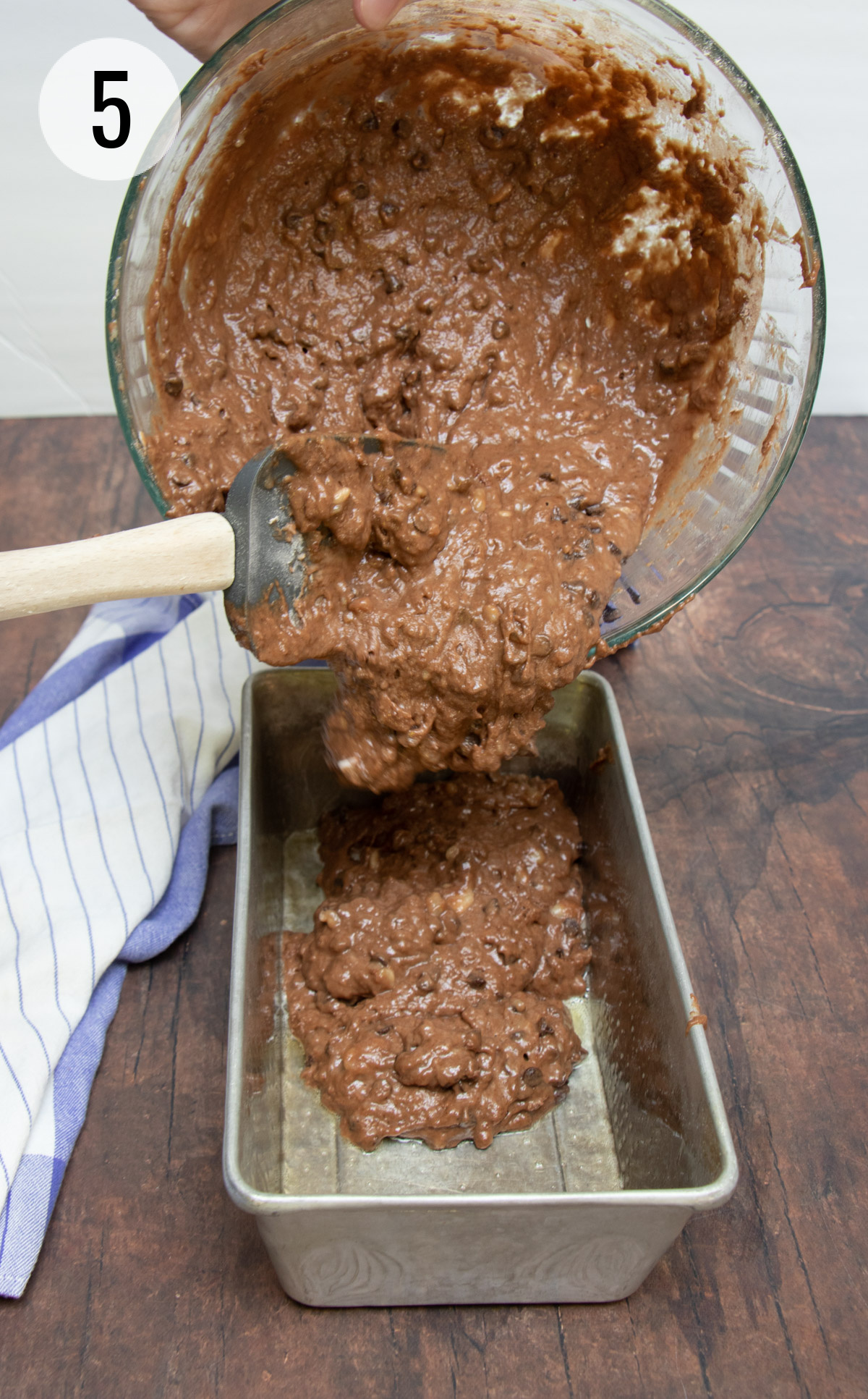 Spreading chocolate chip banana bread batter into a silver loaf baking pan. 