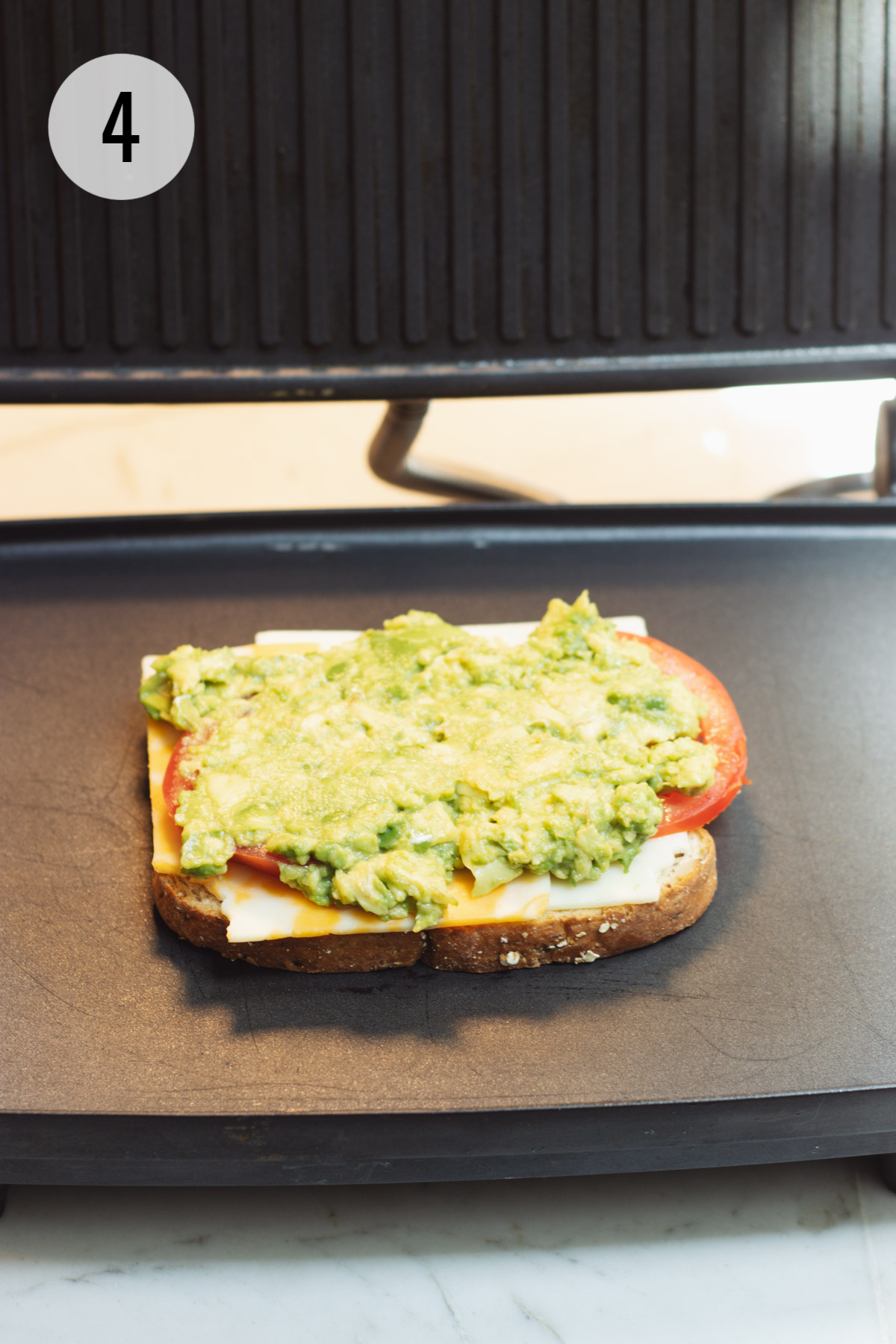 One slice of bread topped with cheese, tomato and avocado on a panini maker.