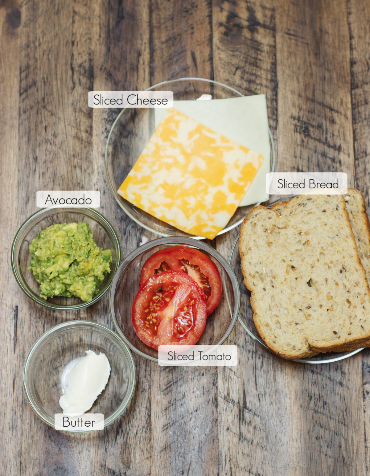 Labeled ingredients in bowls to make a tomato and avocado grilled cheese sandwich.