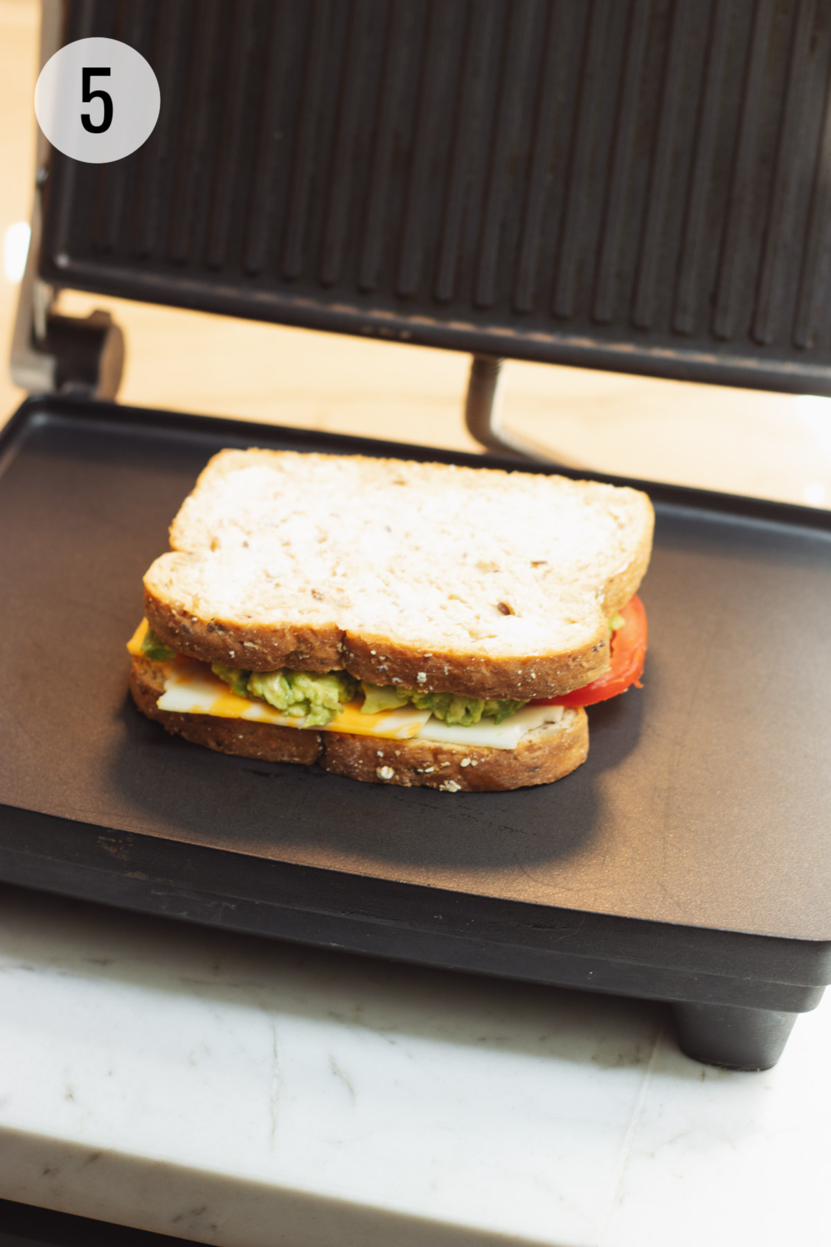 Assembled tomato and avocado grilled cheese sandwich ready to be grilled on panini maker.