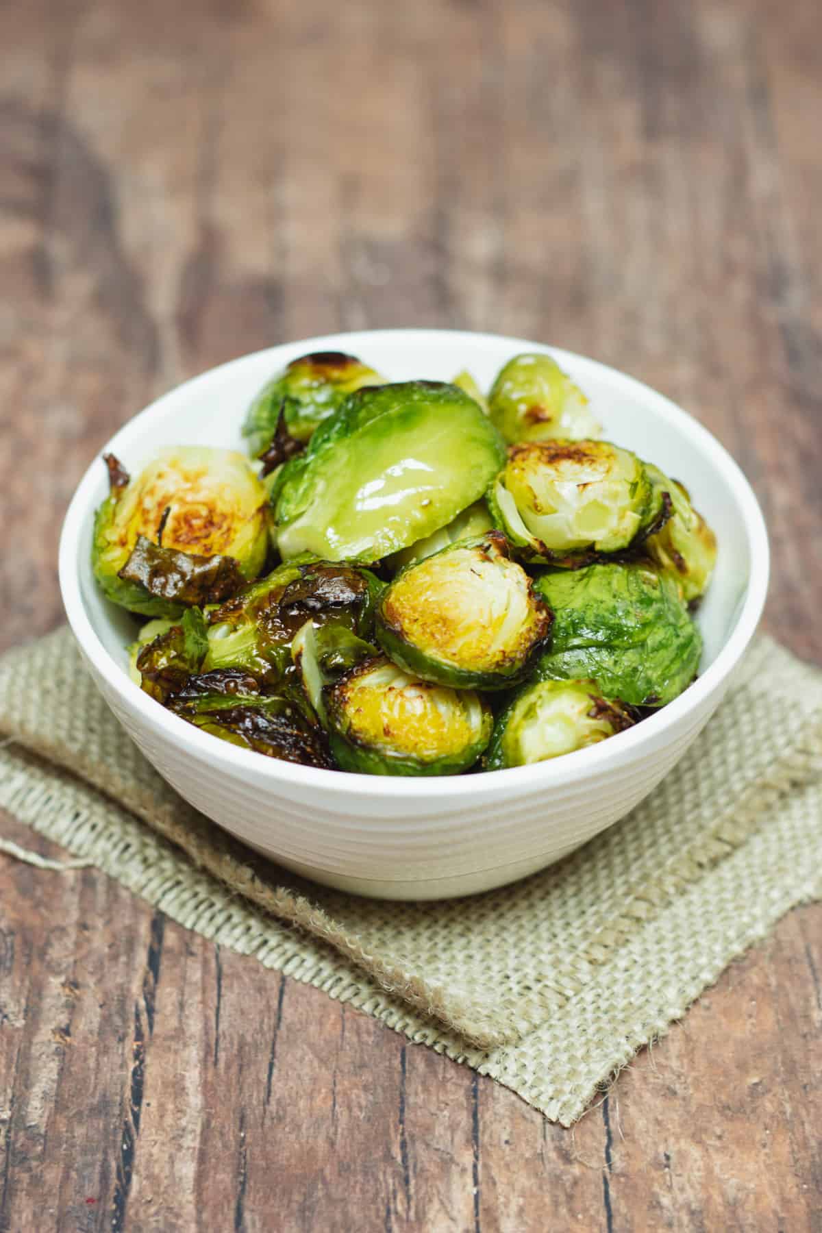 White bowl filled with roasted Brussels sprouts halves on a brown burlap napkin. 