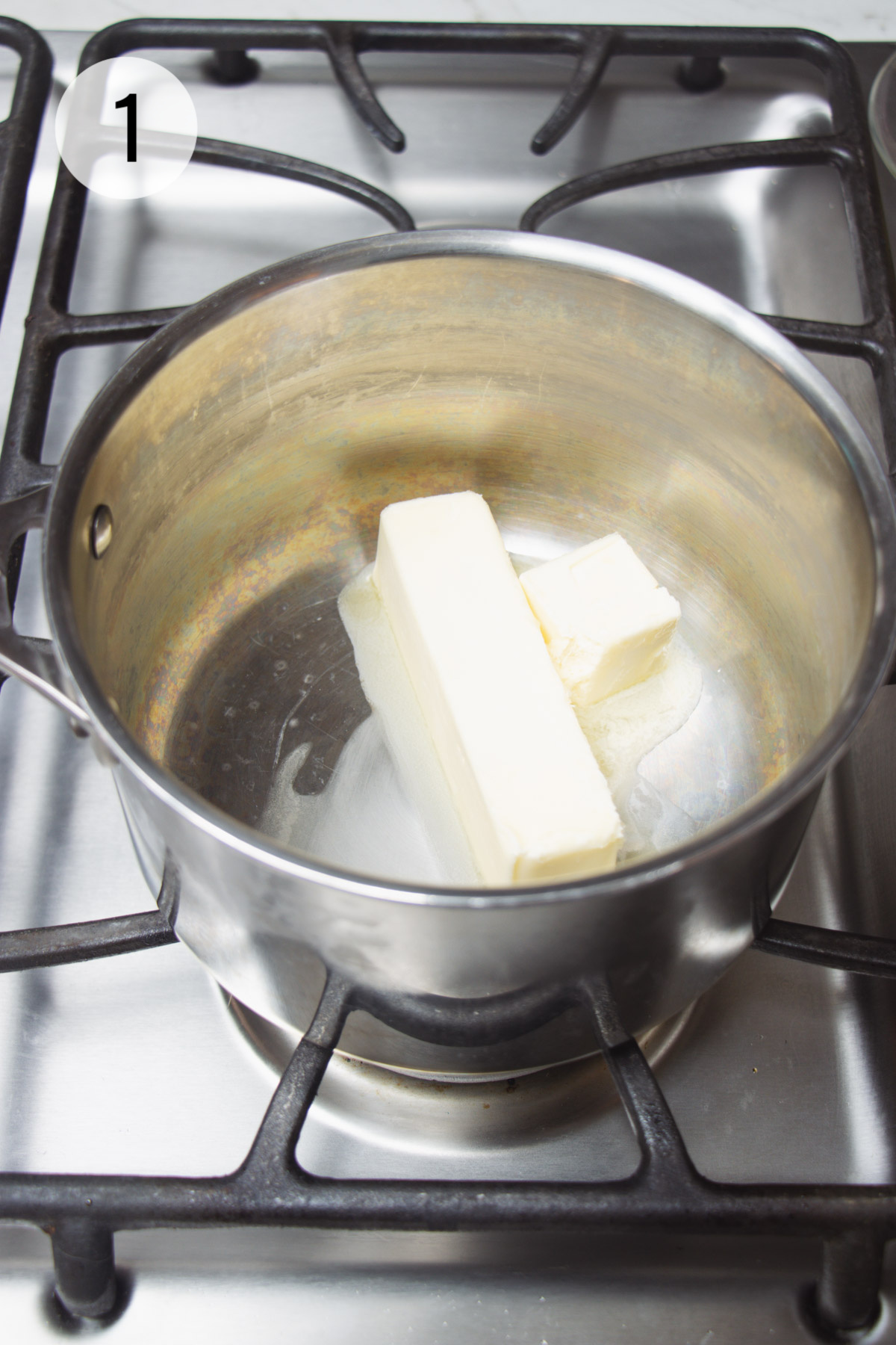 Silver saucepan with stick of butter melting on stove. 