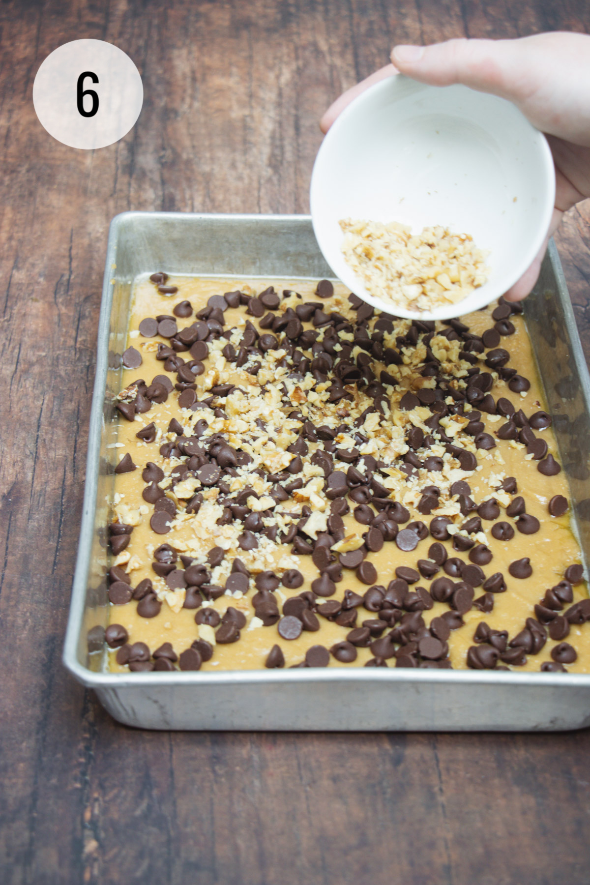 Sprinkling chocolate chips and chopped walnuts on blondie bars batter in a baking pan. 