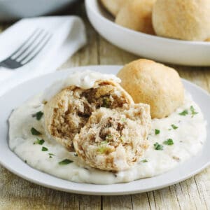 biscuit filled with tuna mixture on plate of creamy mushroom gravy with more biscuits in bowl in background