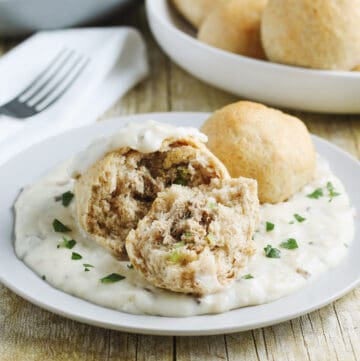 biscuit filled with tuna mixture on plate of creamy mushroom gravy with more biscuits in bowl in background