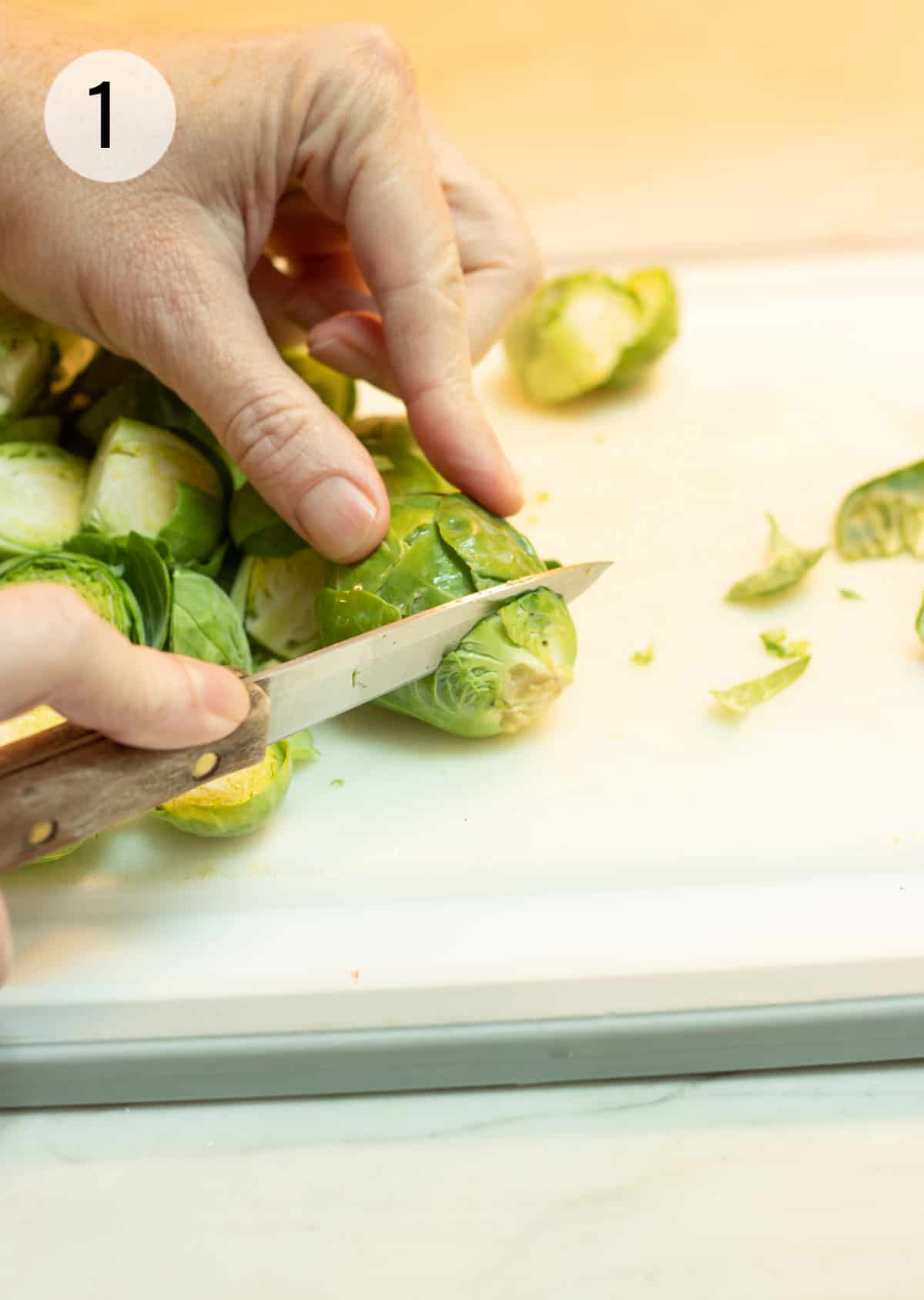 Hand holding a Brussels sprout while small knife is cutting of the end of the stem. 