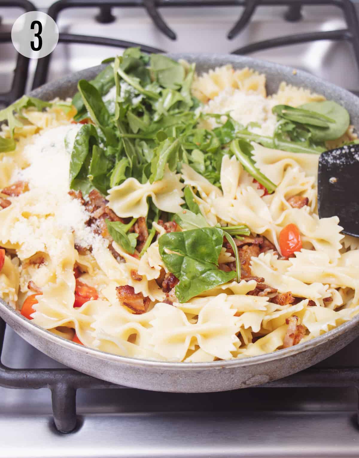 Skillet with baby spinach leaves, bow-tie pasta, chopped bacon and tomatoes.