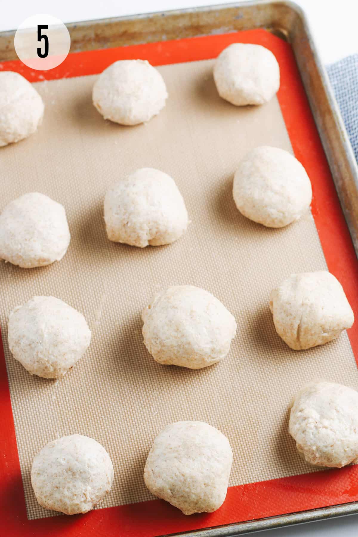 Round balls of tuna filled biscuit dough on a silicone baking mat and baking tray. 