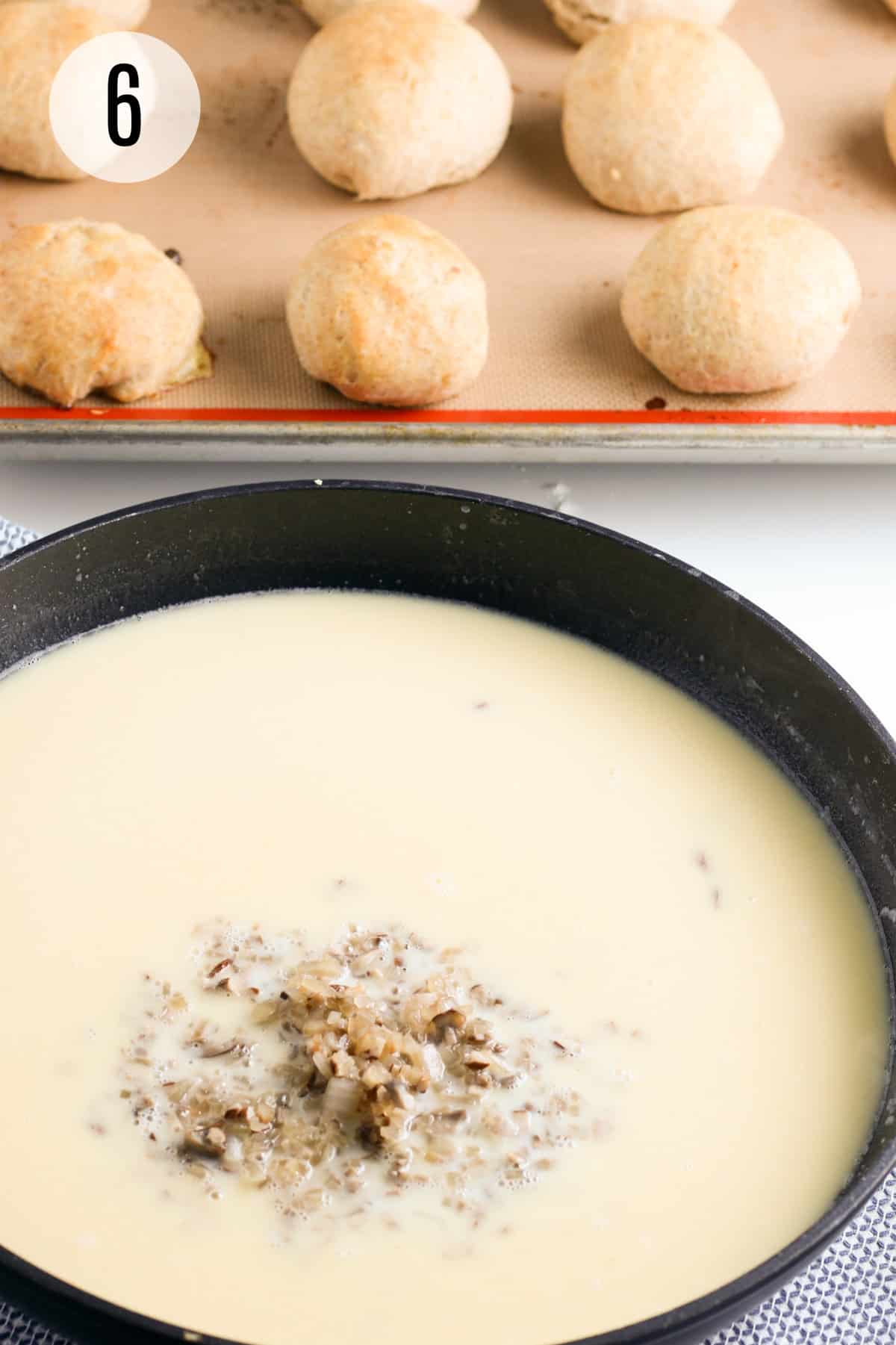 Skillet with creamy mushroom gravy ingredients and mound of chopped onions and mushrooms in background and tray of tuna biscuit pockets in upper background.