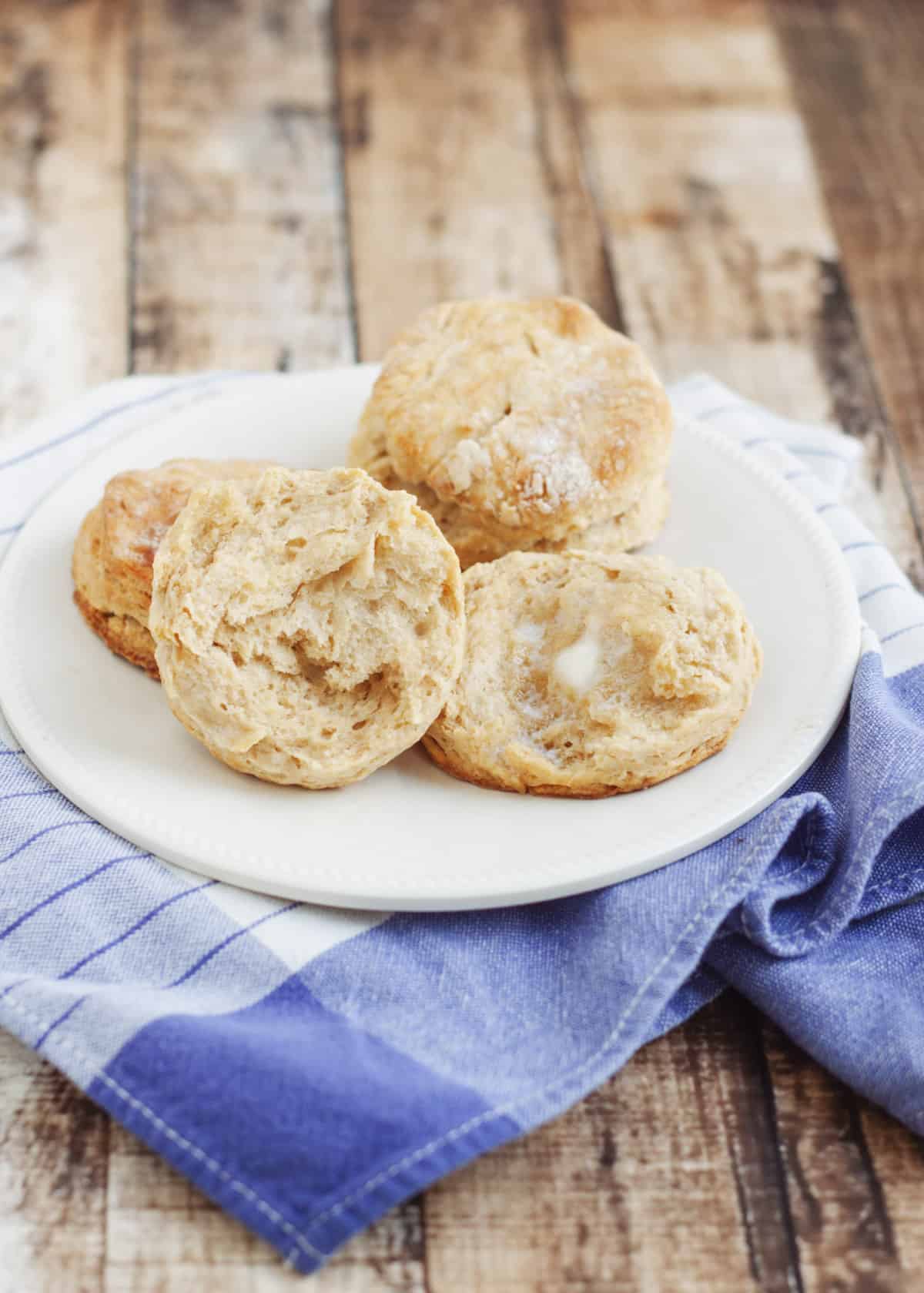 Plate of whole wheat buttermilk biscuits, one cut open with butter melting--on a blue and white tea towel.