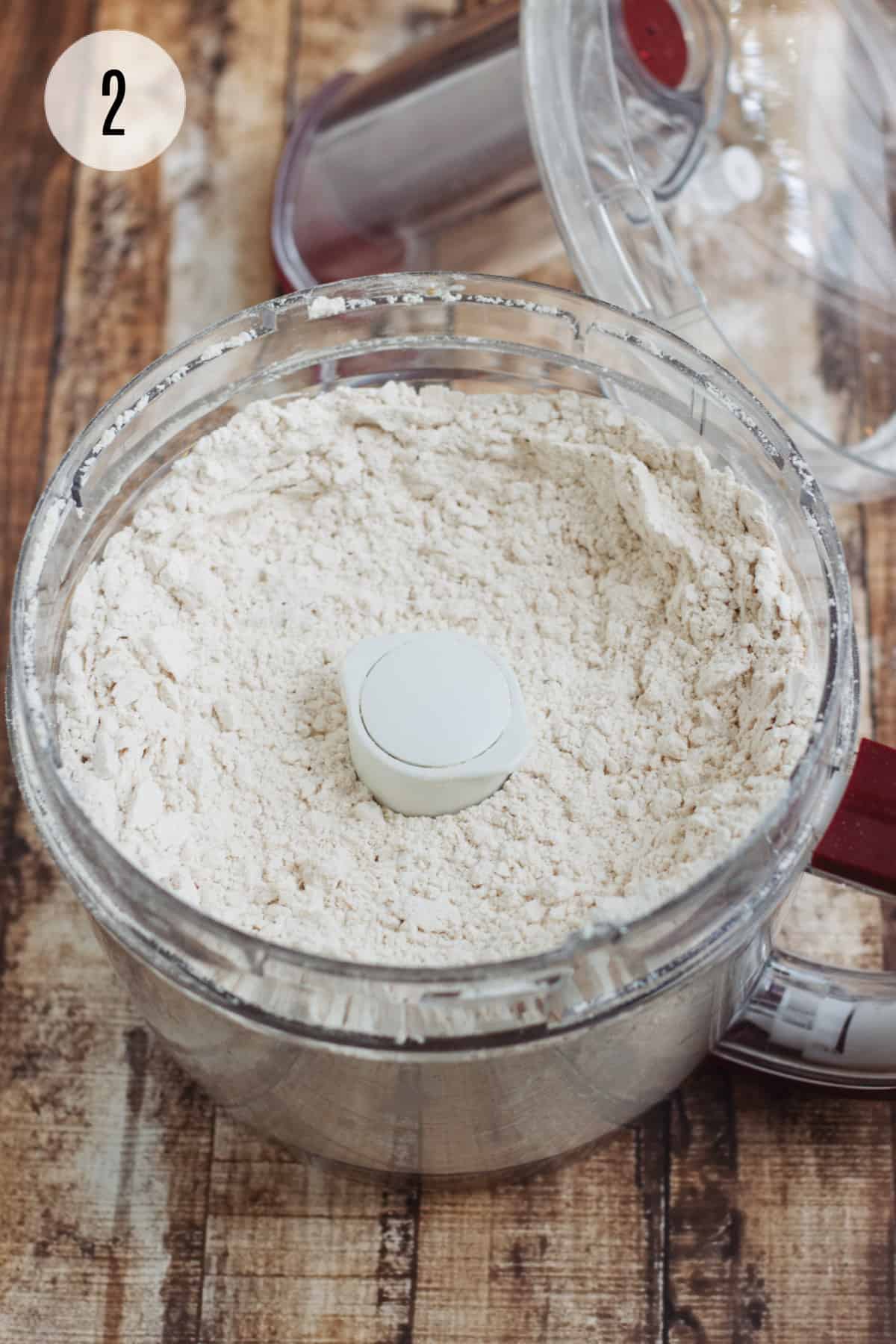 Bowl of food processor with crumbly biscuit mixture and lid in upper right. 