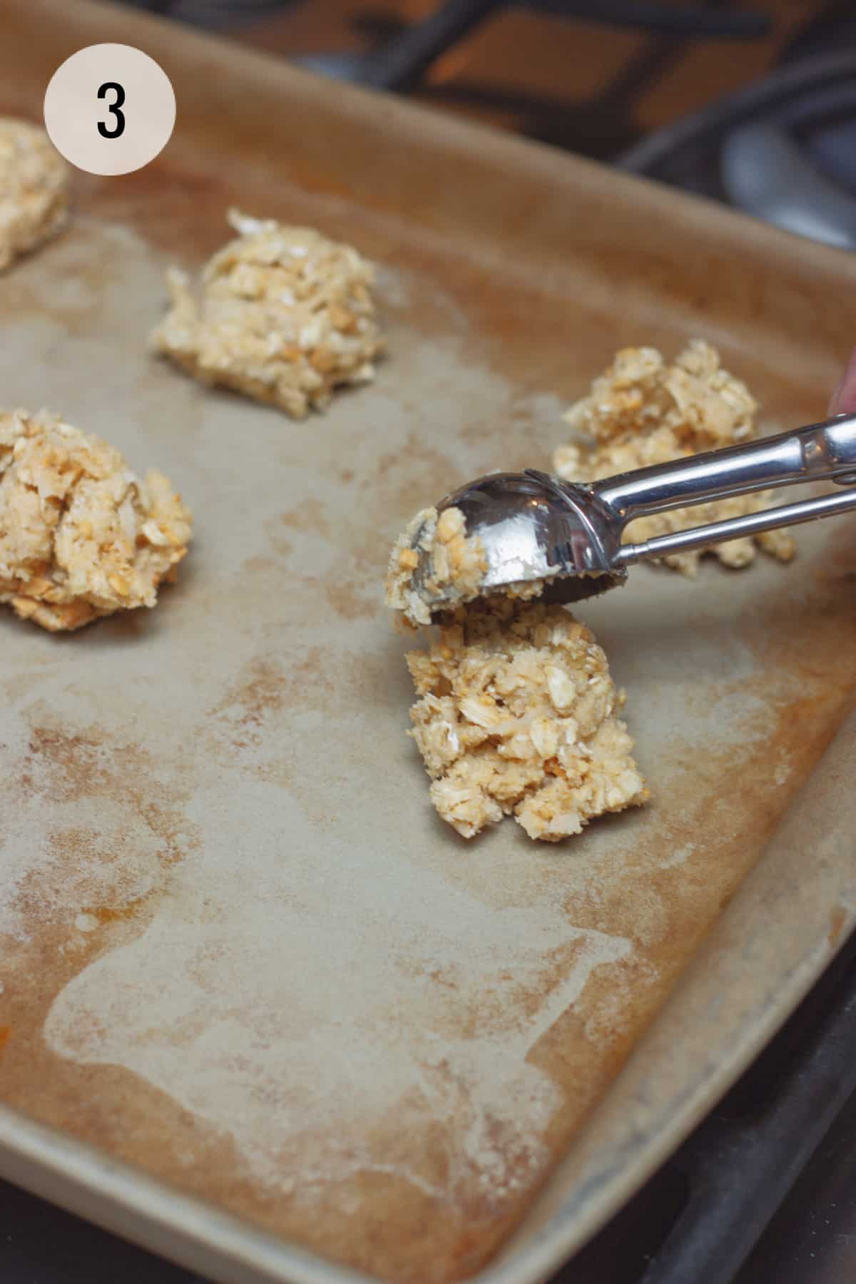 Scooping cookie dough on to a stoneware baking sheet with other dough balls in background. 
