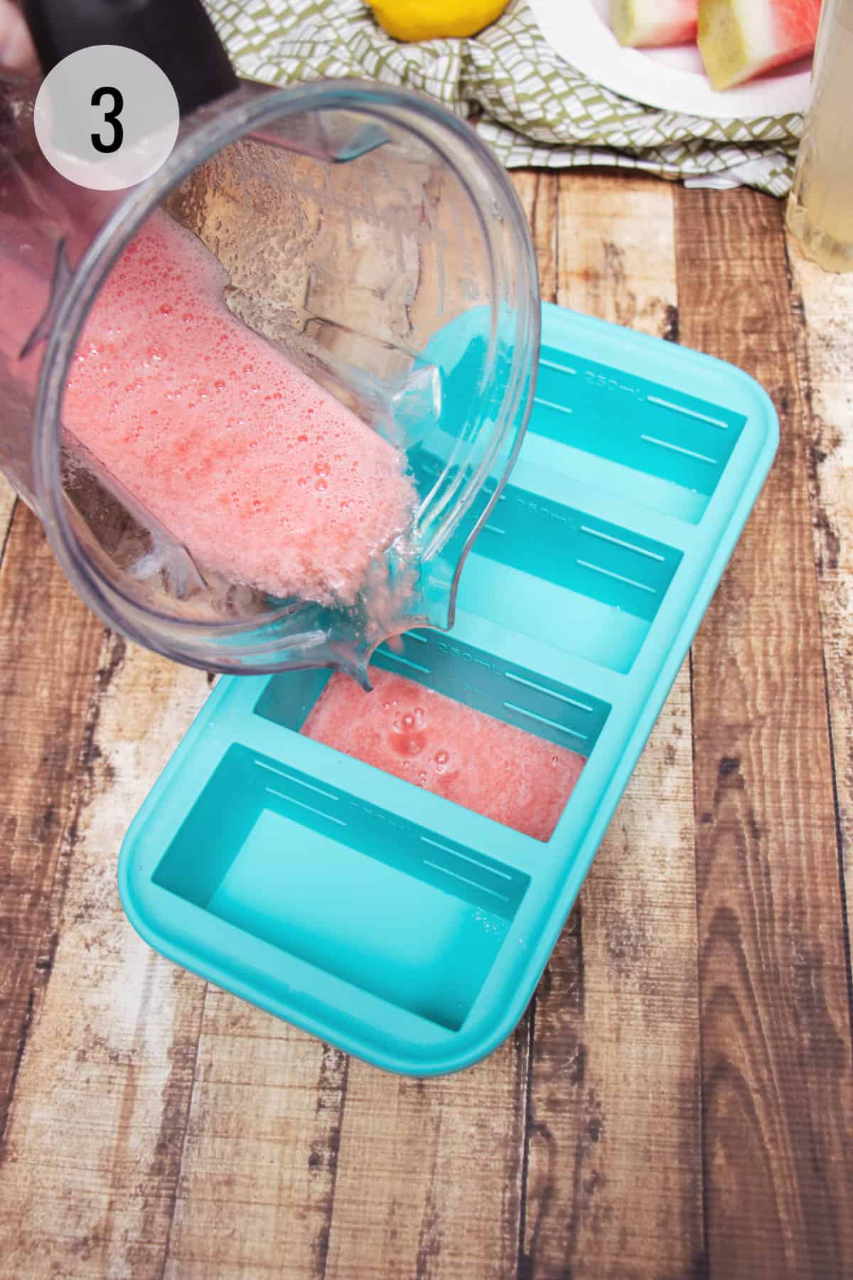 Blender jar pouring pureed watermelon lemonade juice into a blue SouperCubes tray for freezing.