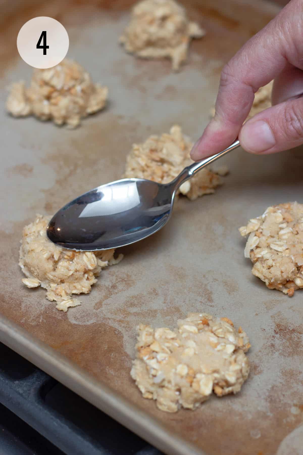 Large silver spoon flattening cookie dough on a baking sheet with other cookie dough portions also. 