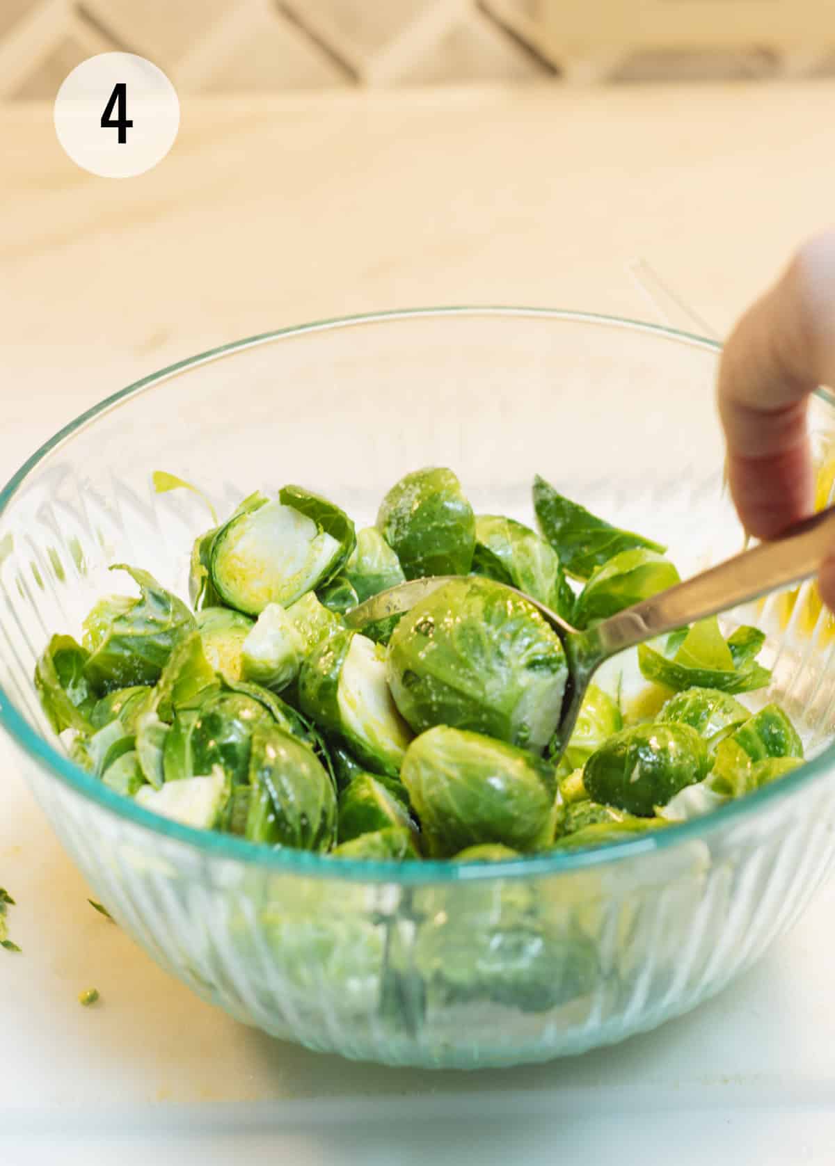 Silver spoon stirring Brussels sprouts halves in a glass bowl.