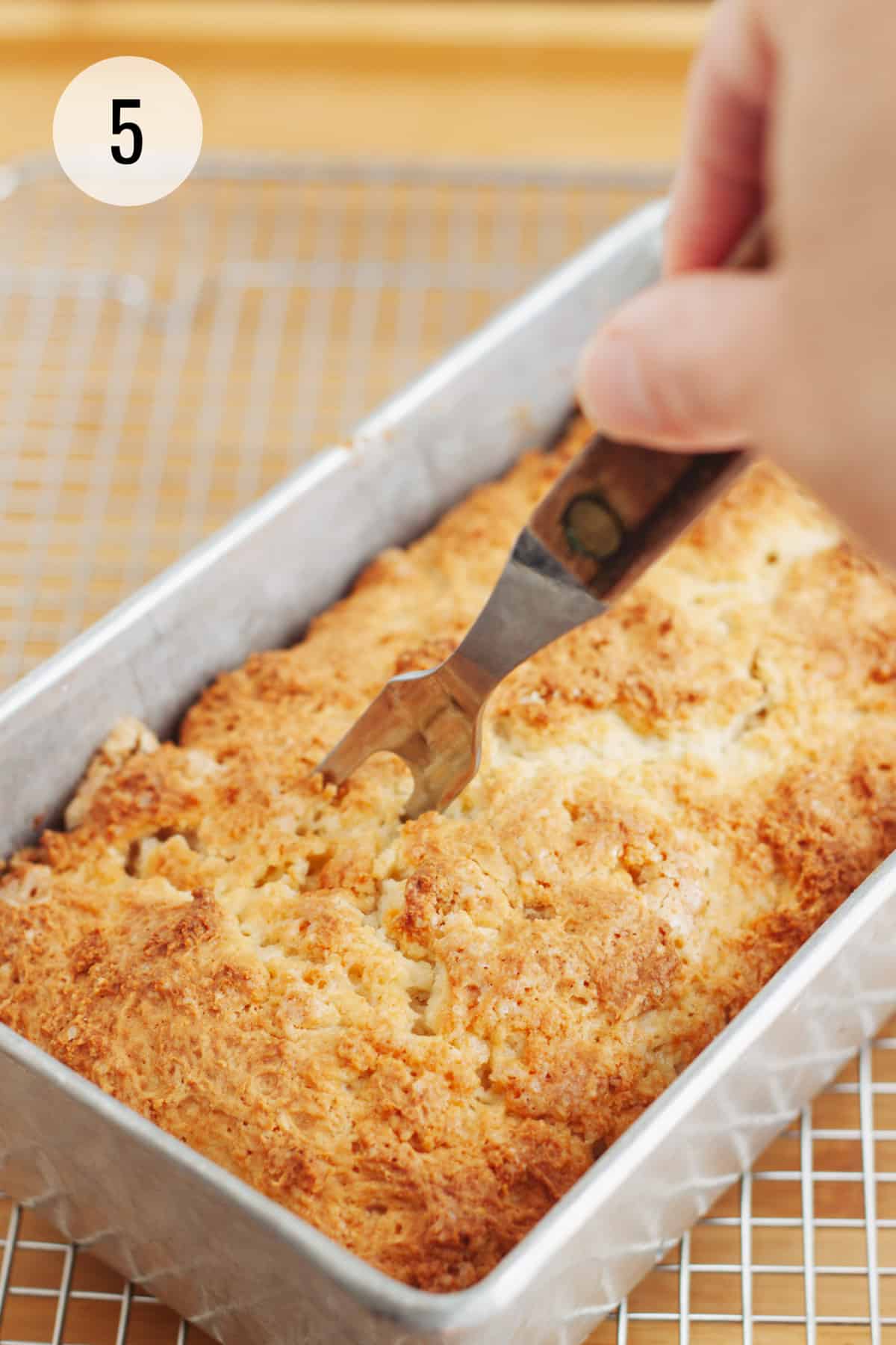 Baked lemon bread with metal fork poking holes in bread. 