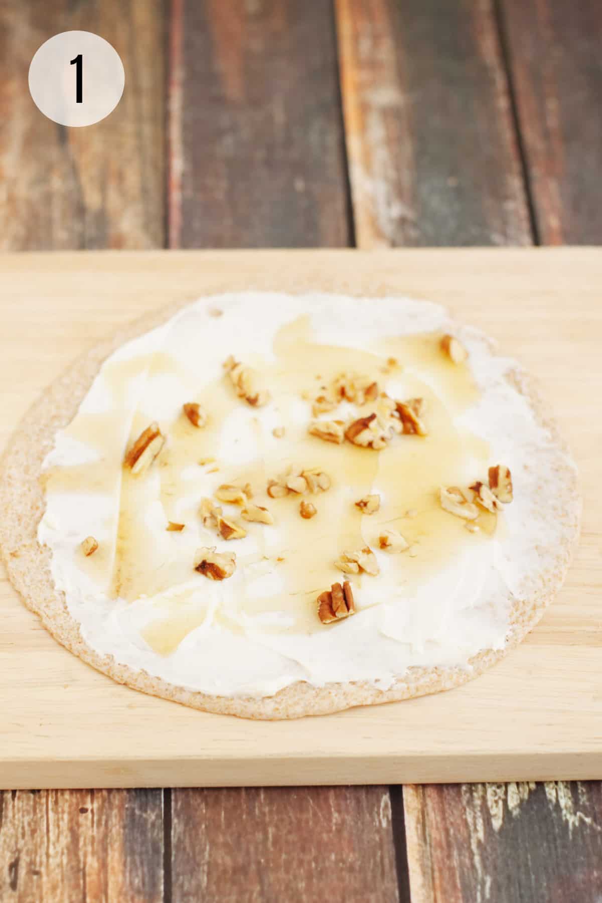 Whole wheat tortilla with cream cheese, honey and pecans on a wooden cutting board with step number at top left.