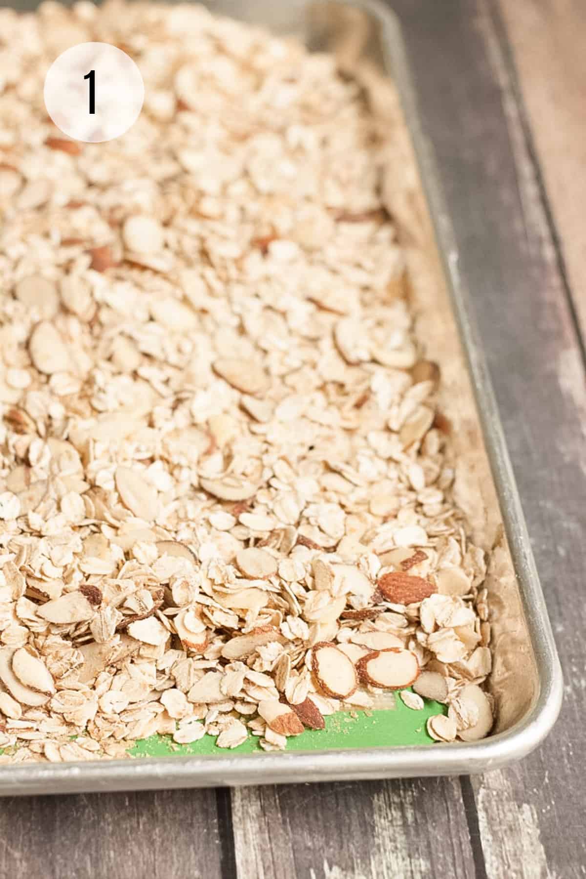 Sliced almonds and oats on a silver baking sheet with green silicone baking mat underneath. 