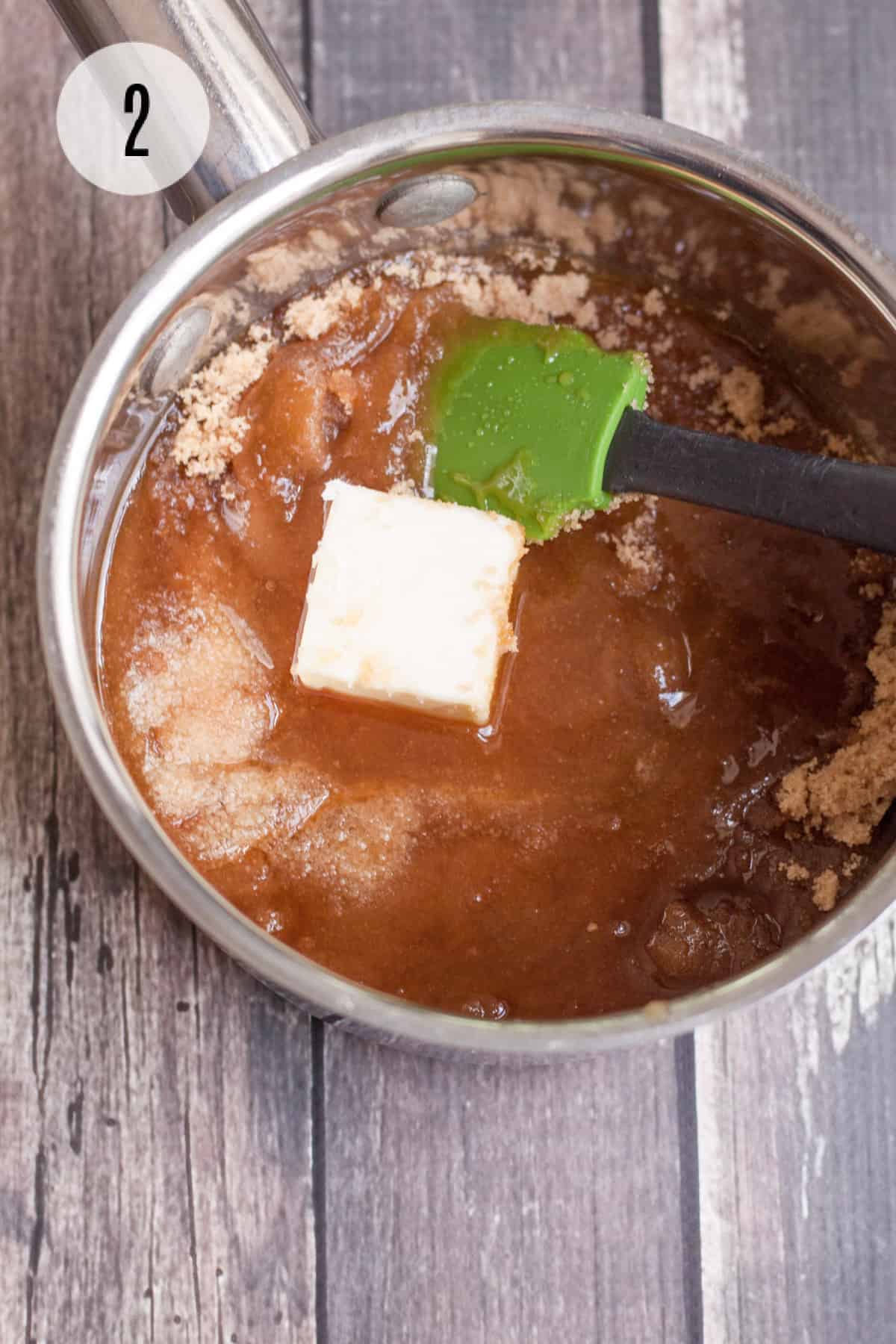 Saucepan with honey, brown sugar and butter mixture stirred by a green and black rubber spatula with step number 2 for homemade granola bars in upper left corner. 