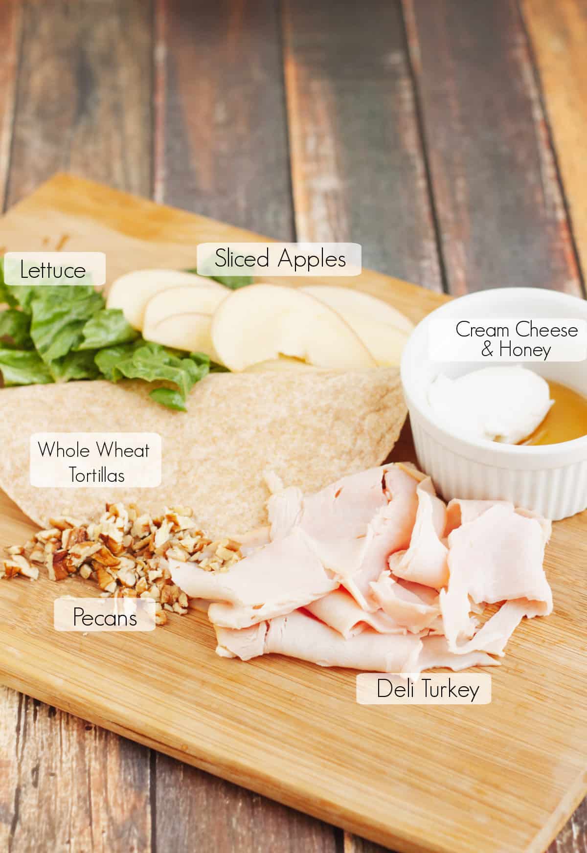 Labeled ingredients on wooden cutting board to make a turkey wrap sandwich. 