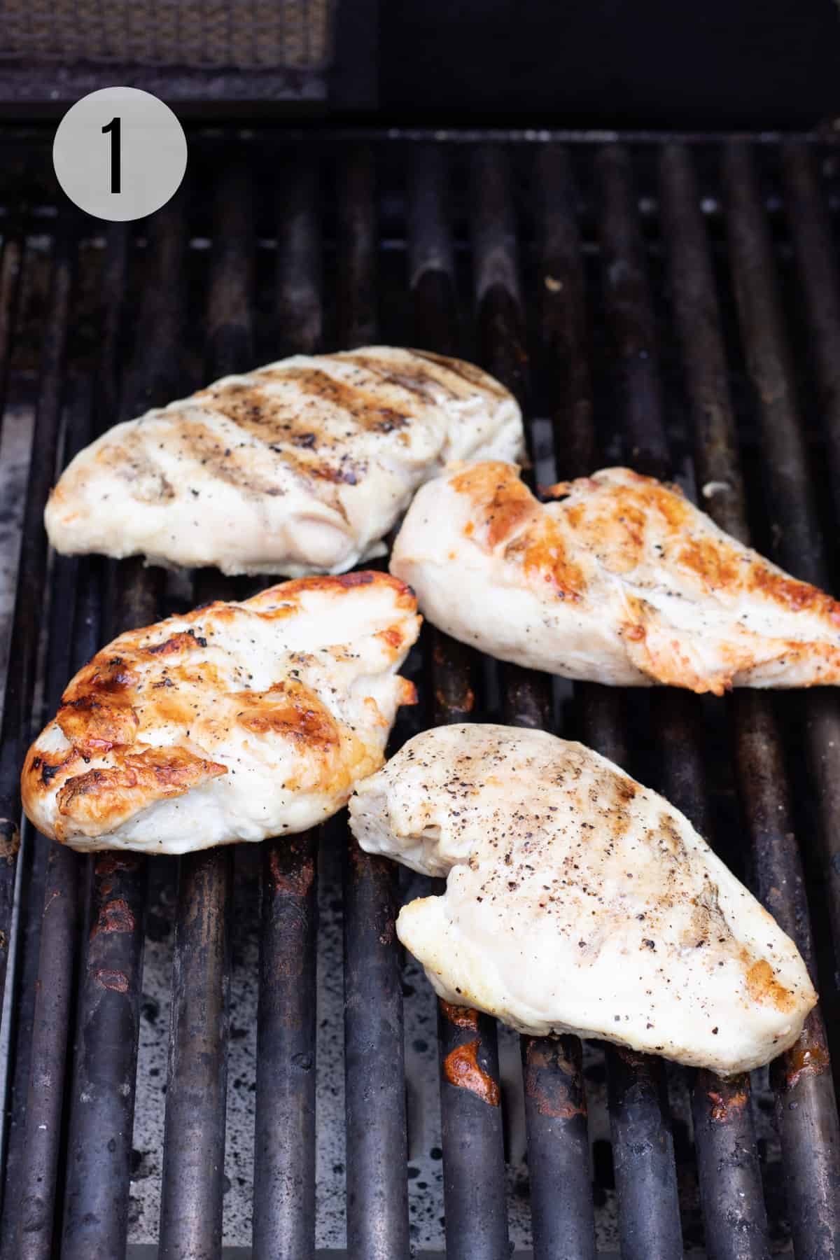 Four boneless chicken breasts on a grill. 