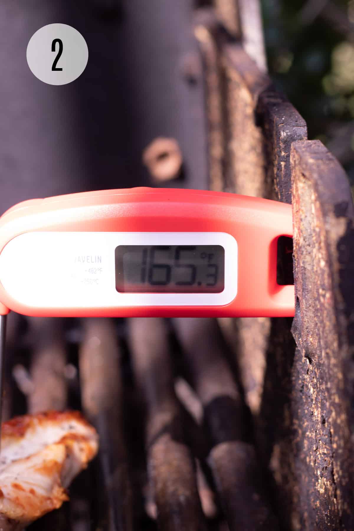 Close up image of a red and white food safe digital thermometer being used on meat on a grill. 