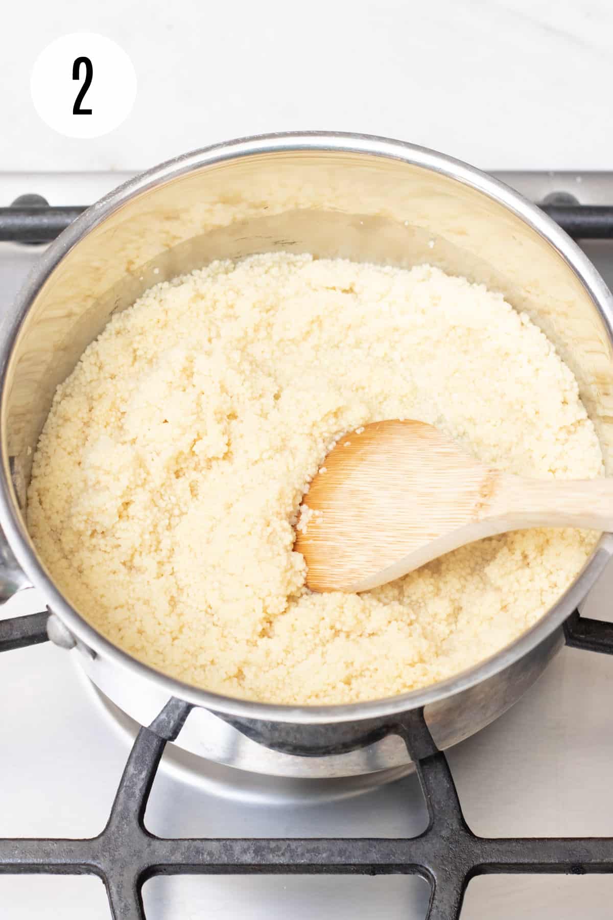 Silver saucepan with wooden spoon stirring couscous on stove. 