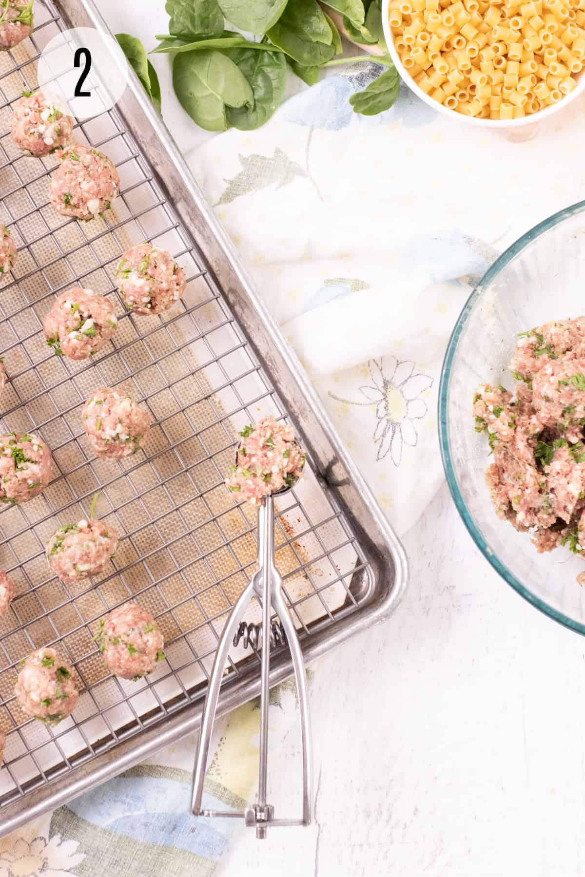 Baking rack on a large sheet pan with tan silicone baking mat and scooped out mini meatballs with bowl of meatball mixture in glass bowl on right. 