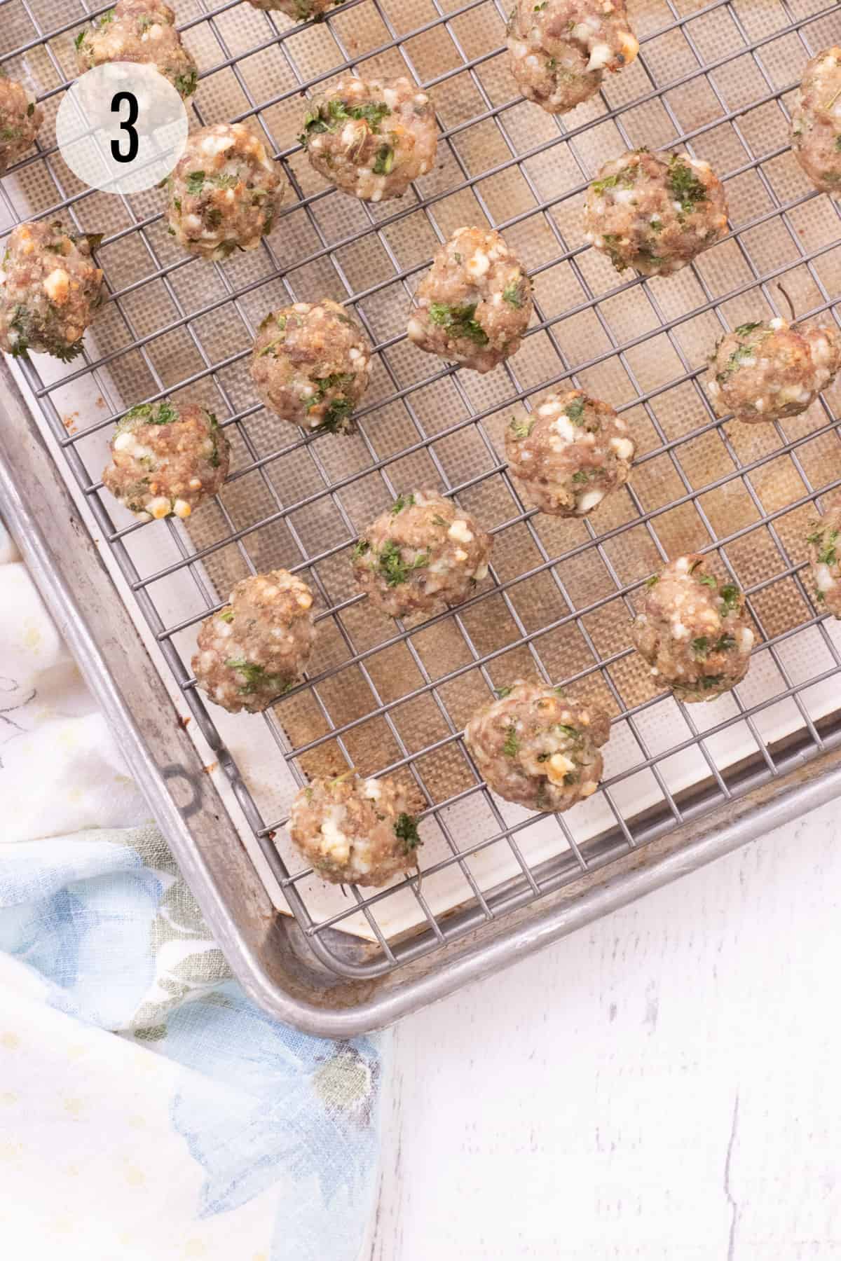 Metal baking rack with tan silicone baking mat on a baking sheet and cooked meatballs with parsley and cheese on baking rack. 