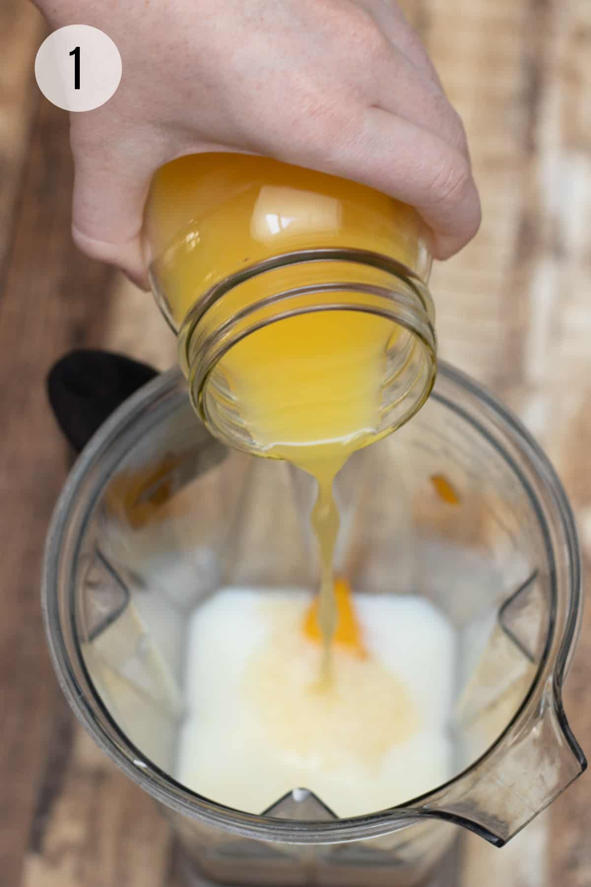Pouring orange juice into blender jar filled with milk, peaches and banana. 