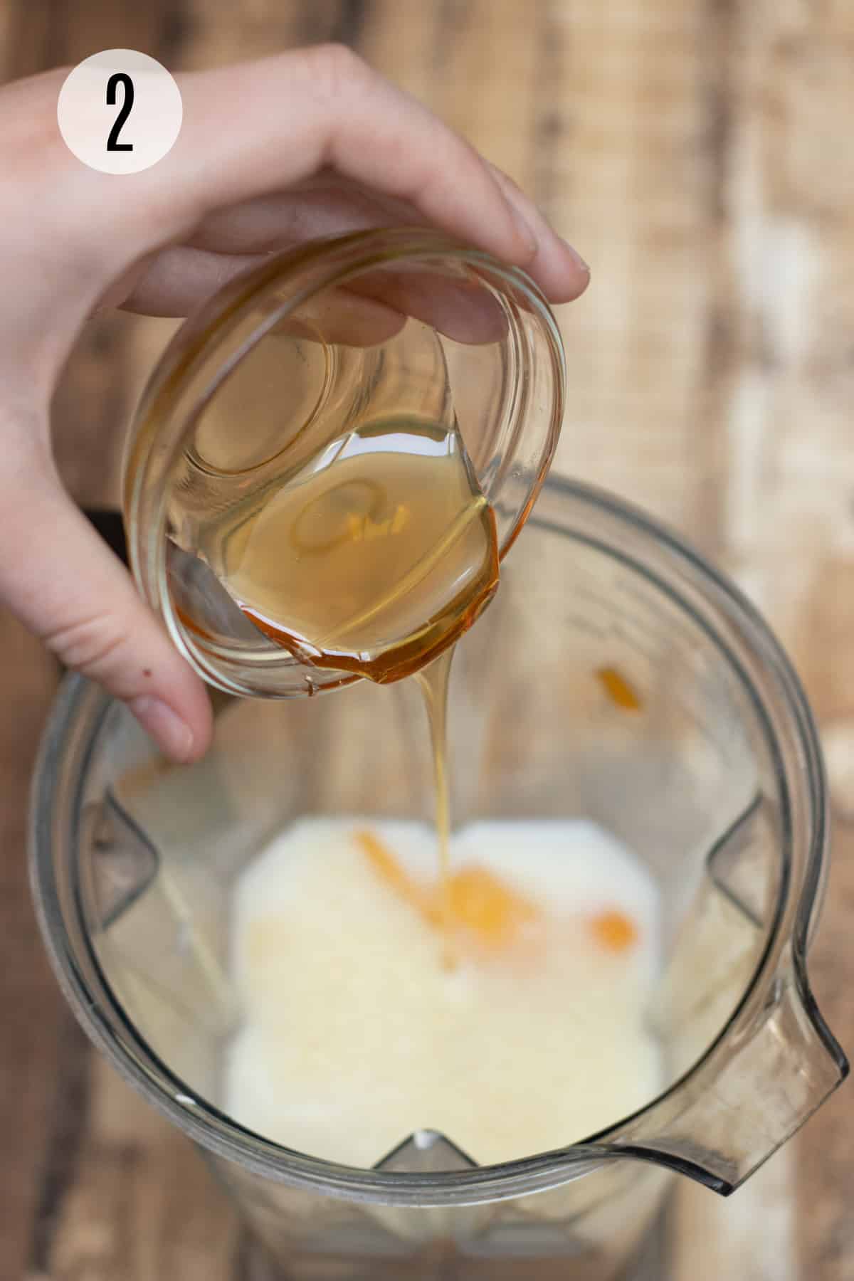 Pouring honey in blender jar filled with peaches, banana and milk. 