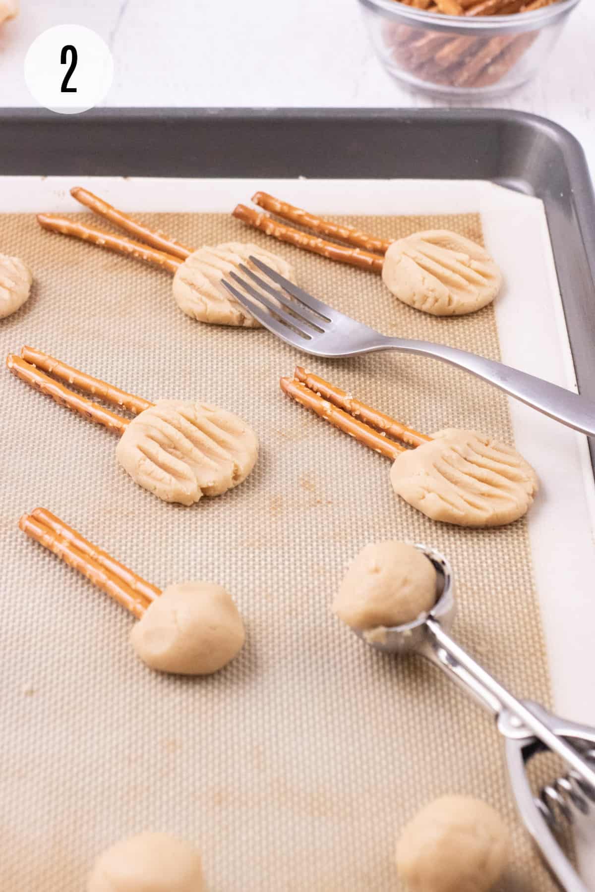 Baking mat with brown sugar shortbread cookie dough balls, metal scoop and pretzels and fork to create witches broom cookie shapes. 