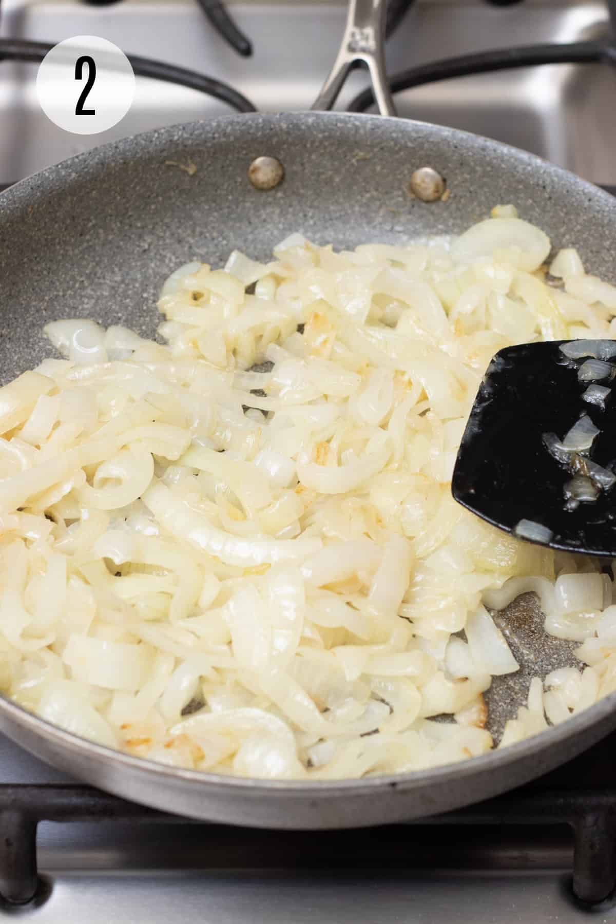 Grey skillet with slightly caramelized sliced onions and black spatula stirring. 