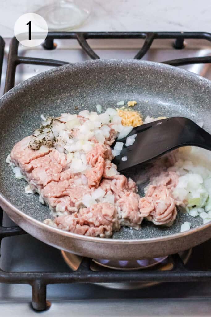 Ground turkey, chopped onion. salt, pepper, dried basil and minced garlic cooking in skillet with black spatula.