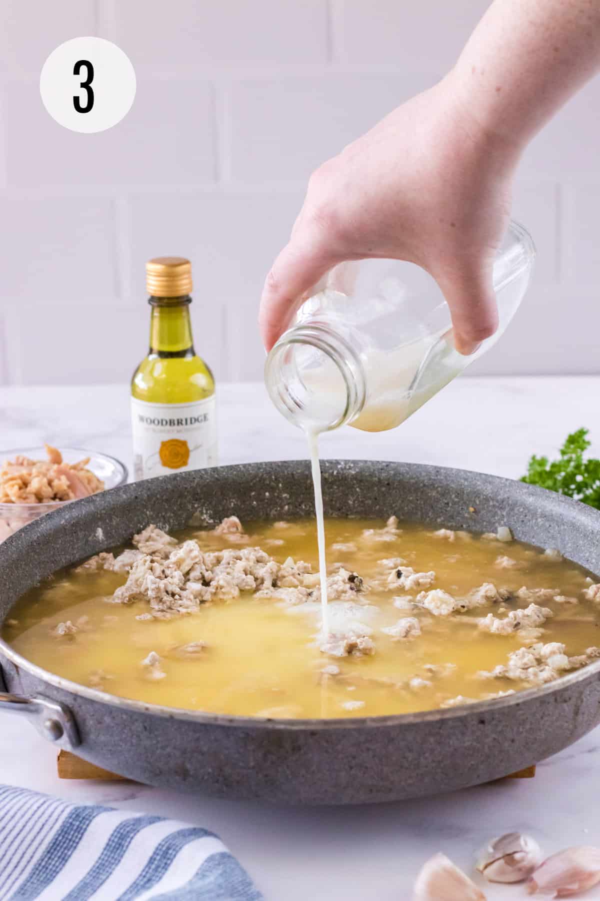 Grey skillet with ground turkey mixture and chicken broth and pouring milk into sauce with other ingredients surrounding. 