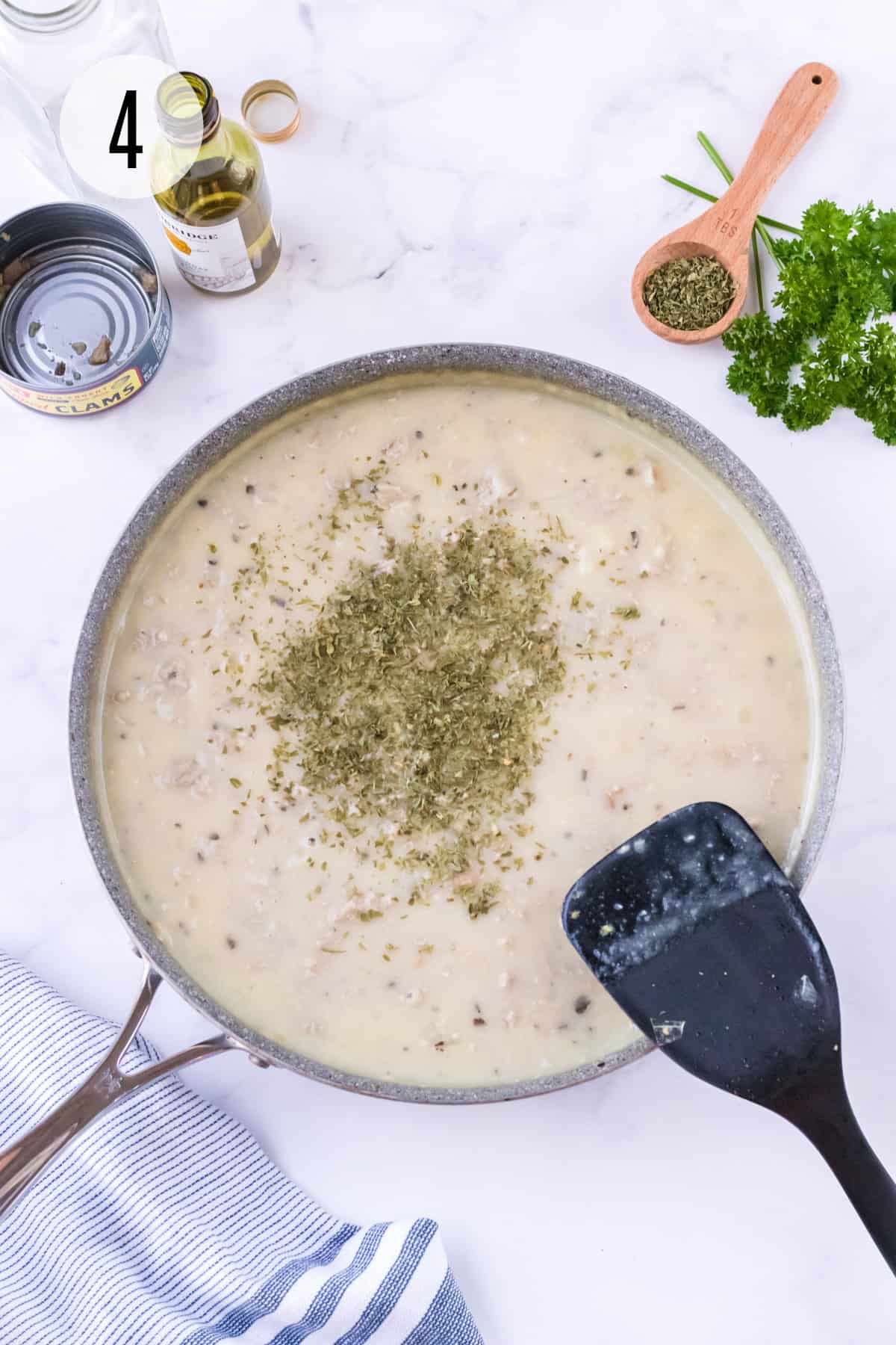 Creamy ground turkey and clam sauce in skillet with dried parsley sprinkled on top with black spatula stirring and additional ingredients in upper background. 