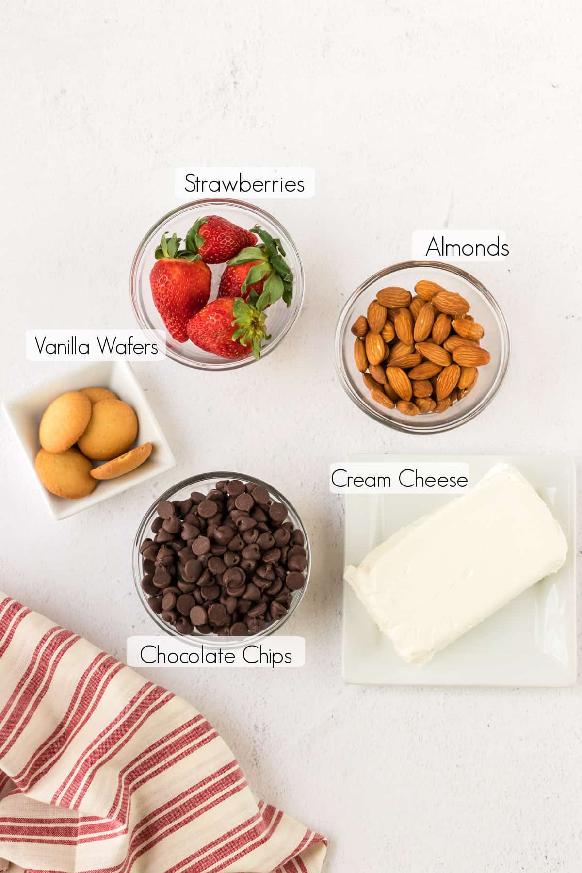 Labeled ingredients to make Strawberry Chocolate Cheesecake Bites with red and white linen in lower left corner. 